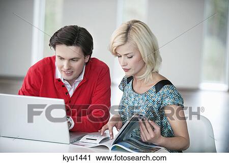 Stock Image - Man using a laptop with a woman reading a magazine. Fotosearch