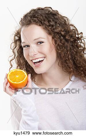 Stock Photo - Portrait of a woman holding a half of an orange and laughing. Fotosearch
