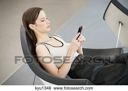 Woman reclining in a chair and text messaging with a mobile phone View Large Photo Image Stock Photo - Woman reclining in a chair and text messaging with a mobile phone. Fotosearch