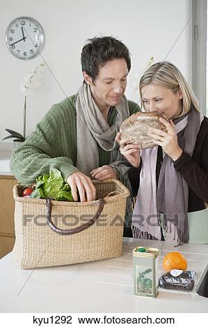 Stock Image - Woman smelling a loaf of bread with her husband standing beside her. Fotosearch