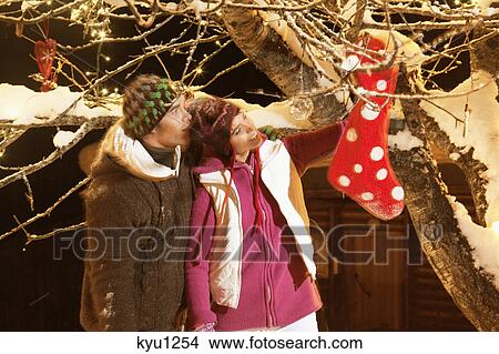 Young couple with Christmas stocking hanging on tree View Large Photo Image Picture - Young couple with Christmas stocking hanging on tree. Fotosearch