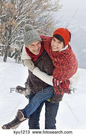 Stock Image - Young man giving his girlfriend piggyback in snow. Fotosearch