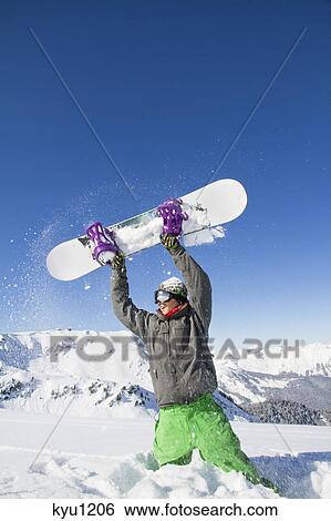 Young man holding his snowboard above his head View Large Photo Image Stock Photograph - Young man holding his snowboard above his head. Fotosearch