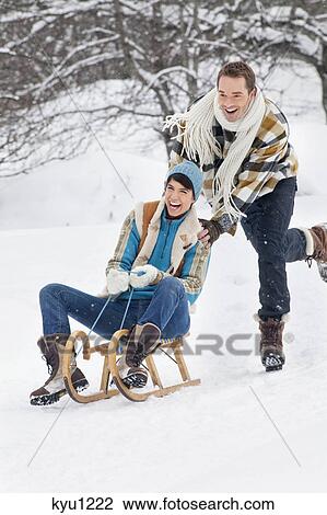 Stock Image - Young man pushing woman on sled. Fotosearch