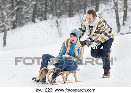 Young man pushing woman on sled View Large Photo Image Stock Image - Young man pushing woman on sled. Fotosearch