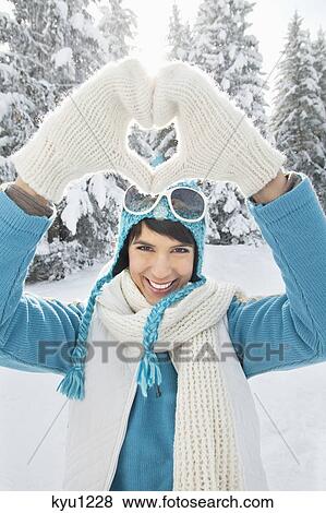 Stock Photo - Young woman in winter clothes making heart shape with hands. Fotosearch