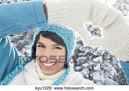 Stock Photo - Young woman in winter clothes making heart shape with hands. Fotosearch