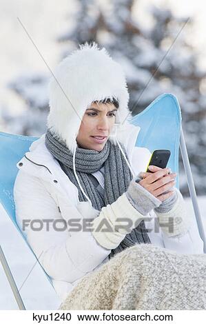 Stock Image - Young woman using mobile phone in snow. Fotosearch