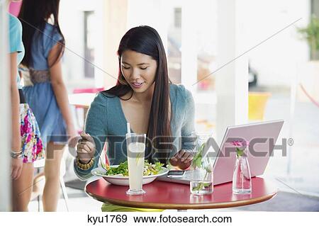 Stock Photo - Beautiful woman eating food with laptop on table in a restaurant. Fotosearch