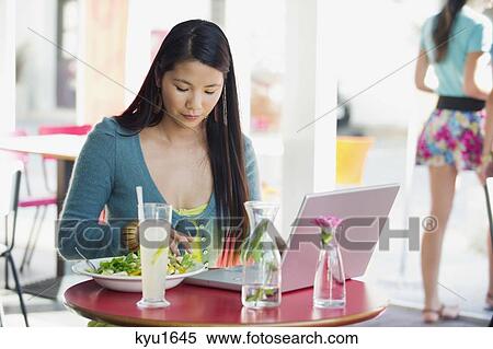 Stock Photography - Beautiful woman eating food with laptop on table in a restaurant. Fotosearch