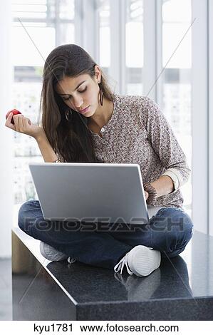 Beautiful woman holding an apple while using a laptop View Large Photo Image Stock Image - Beautiful woman holding an apple while using a laptop. Fotosearch