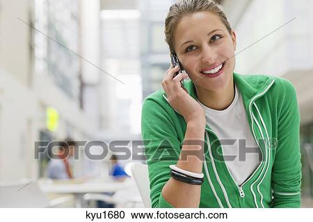 Stock Image - Beautiful woman talking on a mobile phone in university lobby. Fotosearch