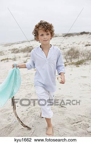 Stock Image - Boy holding flag and walking on beach. Fotosearch