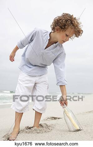 Boy reaching for message in a bottle on beach View Large Photo Image Stock Photograph - Boy reaching for message in a bottle on beach. Fotosearch