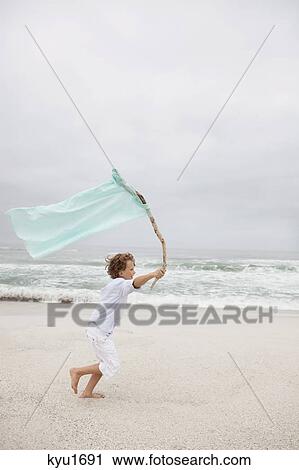 Boy running while holding flag on beach View Large Photo Image Stock Image - Boy running while holding flag on beach. Fotosearch