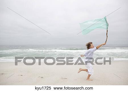 Stock Photography - Boy running while holding flag on beach. Fotosearch