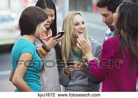 Friends using mobile phones outdoors View Large Photo Image Stock Image - Friends using mobile phones outdoors. Fotosearch