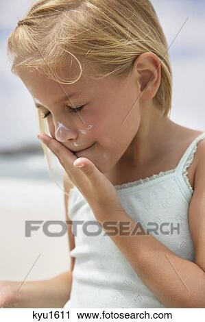 Stock Image - Girl applying sunscreen lotion on her face. Fotosearch