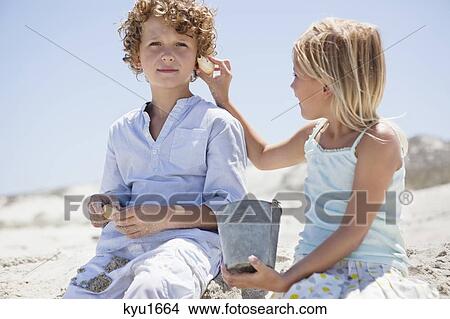 Girl holding shell to her brother's ear on beach View Large Photo Image Picture - Girl holding shell to her brother's ear on beach. Fotosearch