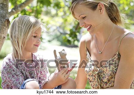 Little girl and her mother looking at toy in hand outdoors View Large Photo Image Picture - Little girl and her mother looking at toy in hand outdoors. Fotosearch