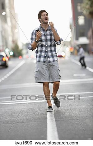 Stock Image - Man talking on a mobile phone while walking on the road. Fotosearch