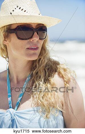 Stock Photography - Mid adult woman wearing sunglasses and sunhat. Fotosearch
