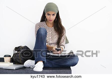Stock Image - Portrait of a beautiful woman using mobile against white background. Fotosearch