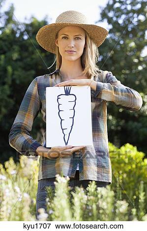 Stock Photo - Portrait of a young woman showing carrot painting in a field. Fotosearch