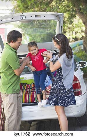 Stock Image - Smiling parents lifting little girl against car. Fotosearch