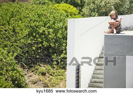 Teenage boy sitting on the edge of a terrace hugging his knees View Large Photo Image Stock Photography - Teenage boy sitting on the edge of a terrace hugging his knees. Fotosearch