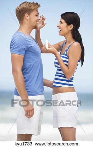 Stock Image - Woman applying suntan lotion on man's face. Fotosearch