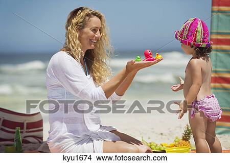 Picture - Woman giving toys to her daughter on the beach. Fotosearch