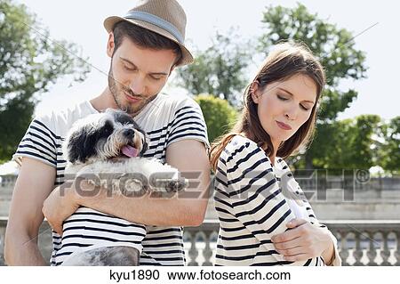 Stock Image - Man carrying a puppy and smiling with a woman looking sad, Paris, Ile-de-France, France. Fotosearch