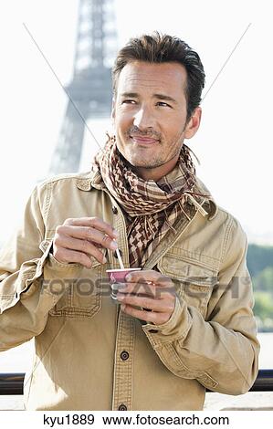 Stock Photo - Man holding a disposable cup with the Eiffel Tower in the background, Paris, Ile-de-France, France. Fotosearch