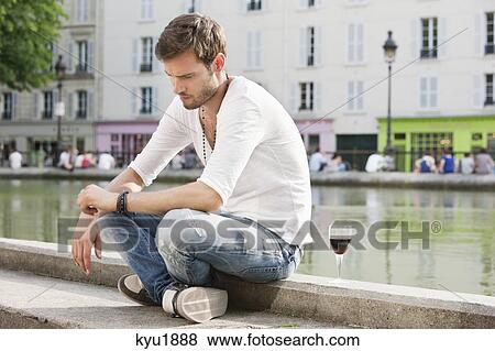 Stock Photo - Man sitting at the ledge of a canal and thinking, Paris, Ile-de-France, France. Fotosearch