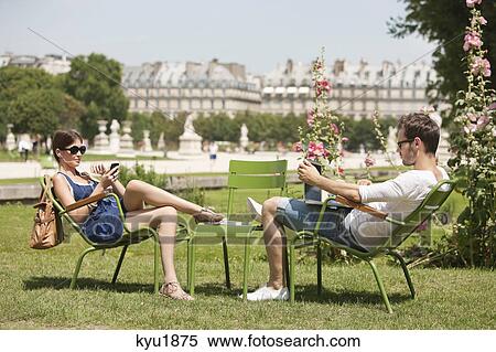 Stock Photography - Man using a laptop with a woman talking on a mobile phone, Jardin des Tuileries, Paris, Ile-de-France, France. Fotosearch