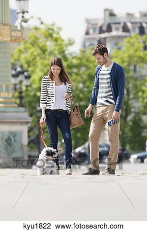 Stock Image - Woman holding a puppy on leash with a man standing beside her, Paris, Ile-de-France, France. Fotosearch