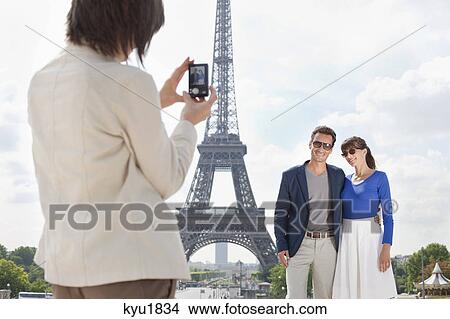 Picture - Woman taking a picture of couple with the Eiffel Tower in the background, Paris, Ile-de-France, France. Fotosearch