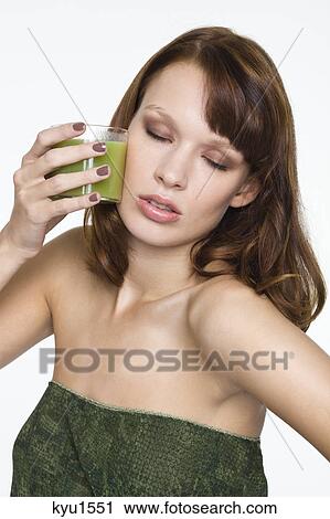 Stock Image - Young woman holding glass of wheatgrass juice. Fotosearch