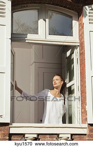 Stock Image - Young woman opening window. Fotosearch