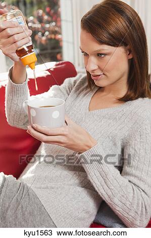 Stock Image - Young woman pouring honey into her tea cup. Fotosearch