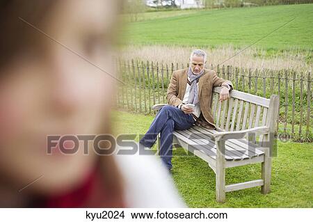 Picture - Close-up of a girl with her father text messaging in the background. Fotosearch