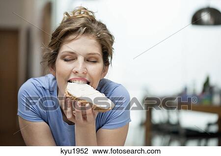 Stock Image - Close-up of a woman eating toast with cream spread on it. Fotosearch