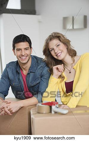 Stock Photo - Couple leaning over cardboard boxes and smiling. Fotosearch