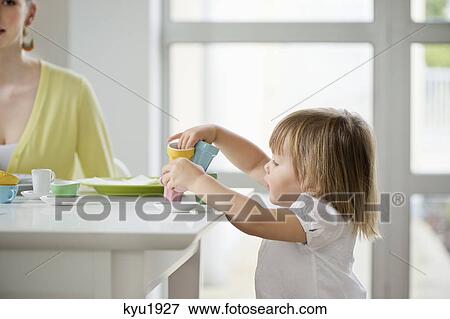 Stock Photo - Cute little girl picking up toy tea set from a dining table. Fotosearch