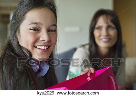 Stock Photo - Girl holding a shopping bag and smiling with her mother. Fotosearch