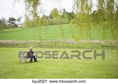 Stock Photo - Man sitting on a bench in a field. Fotosearch