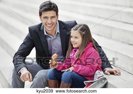 Man sitting with his daughter eating pain au chocolat View Large Photo Image Stock Photo - Man sitting with his daughter eating pain au chocolat. Fotosearch