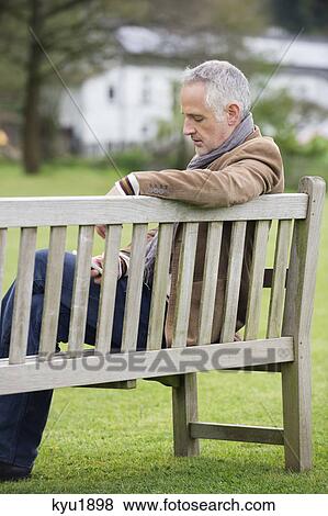 Stock Photo - Man text messaging on a mobile phone in a park. Fotosearch