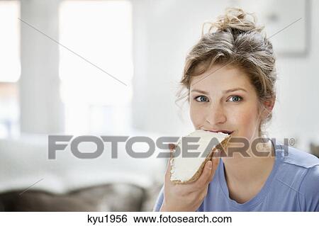 Stock Photograph - Portrait of a woman eating toast with cream spread on it. Fotosearch